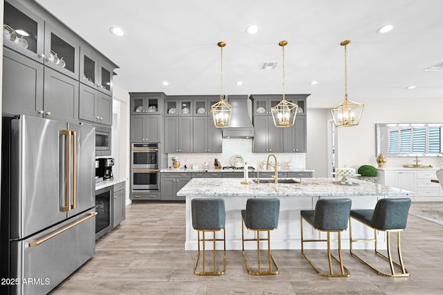 kitchen with decorative backsplash, wall chimney exhaust hood, appliances with stainless steel finishes, gray cabinetry, and a sink