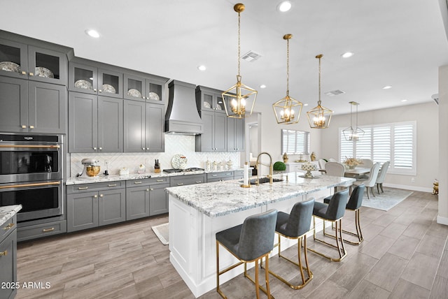 kitchen with stainless steel appliances, custom range hood, visible vents, decorative backsplash, and gray cabinetry