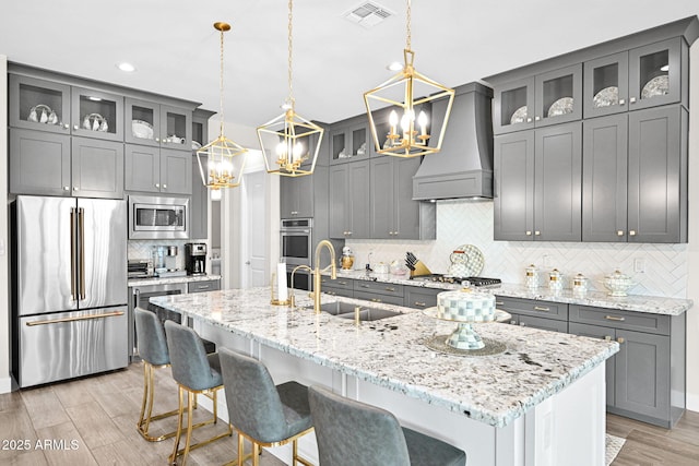 kitchen with visible vents, custom range hood, gray cabinets, stainless steel appliances, and a sink