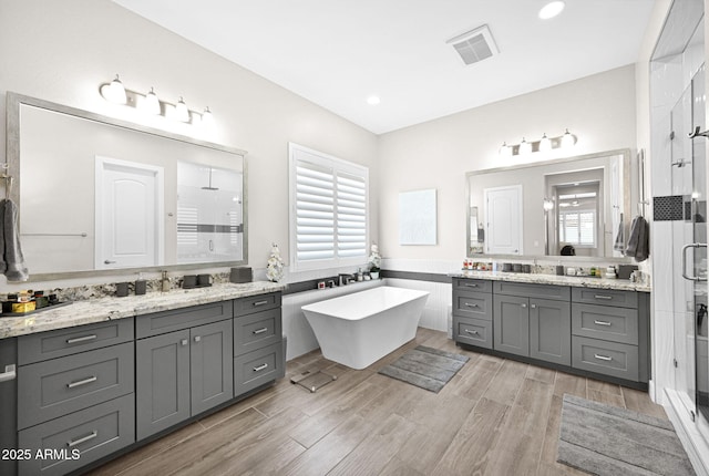 full bath with wood finished floors, plenty of natural light, a shower stall, and visible vents