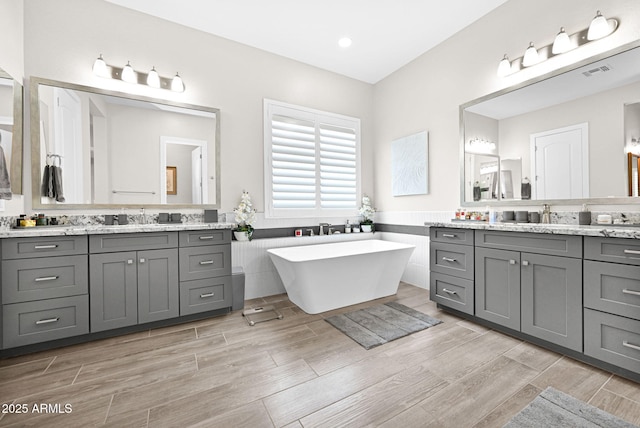 full bathroom with a freestanding bath, two vanities, visible vents, and wood tiled floor