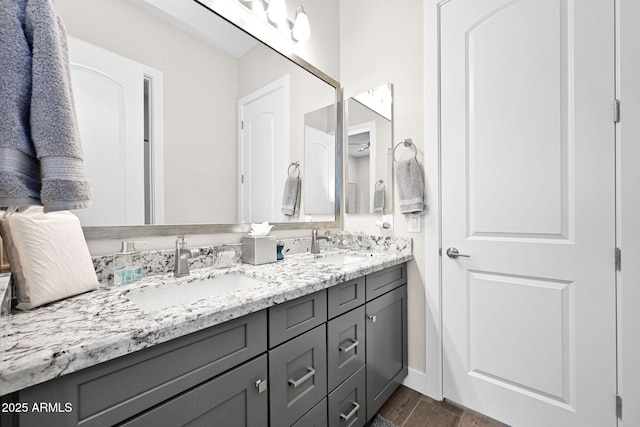 bathroom featuring double vanity, baseboards, a sink, and wood finished floors