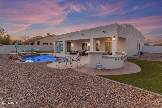 back house at dusk with a fenced in pool, a patio, and an outdoor kitchen