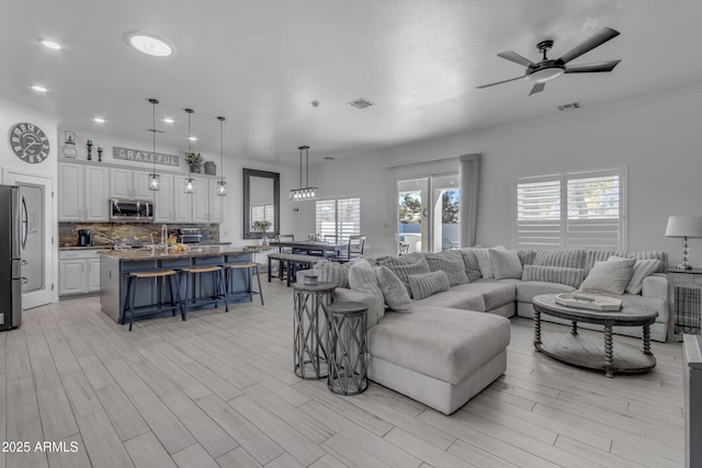 living room with light hardwood / wood-style flooring, ornamental molding, and ceiling fan