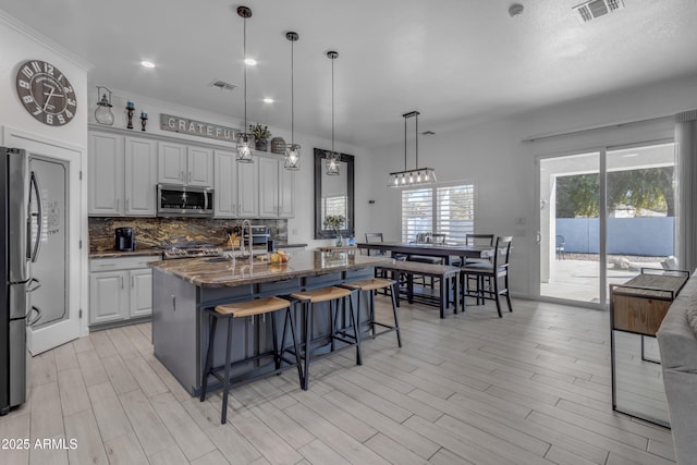 kitchen featuring decorative light fixtures, dark stone countertops, a kitchen breakfast bar, a kitchen island with sink, and stainless steel appliances