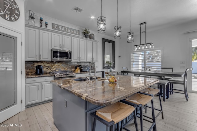 kitchen featuring appliances with stainless steel finishes, sink, dark stone countertops, a kitchen breakfast bar, and a kitchen island with sink