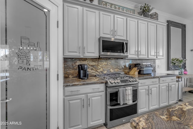 kitchen with crown molding, appliances with stainless steel finishes, dark stone counters, and backsplash