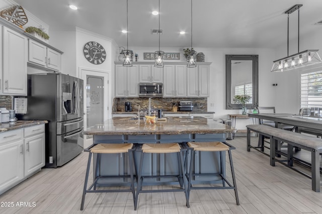 kitchen with a breakfast bar, dark stone countertops, appliances with stainless steel finishes, pendant lighting, and a kitchen island with sink