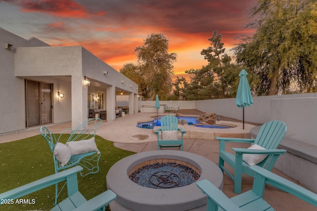 patio terrace at dusk with a fenced in pool and a fire pit