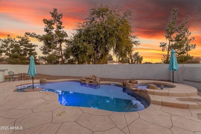 pool at dusk featuring an in ground hot tub and a patio area