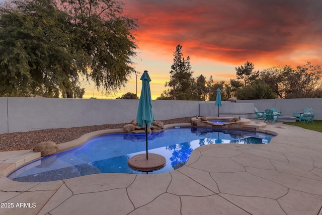 pool at dusk with an in ground hot tub and a patio