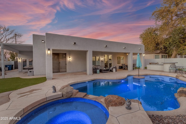 pool at dusk featuring an in ground hot tub, an outdoor kitchen, an outdoor hangout area, and a patio area