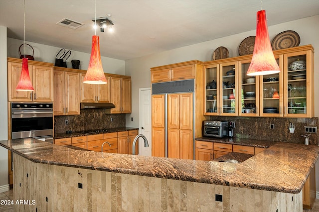 kitchen with pendant lighting, backsplash, sink, paneled built in refrigerator, and dark stone countertops