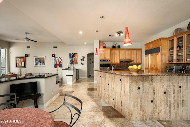 kitchen featuring ceiling fan, hanging light fixtures, paneled refrigerator, tasteful backsplash, and dark stone countertops