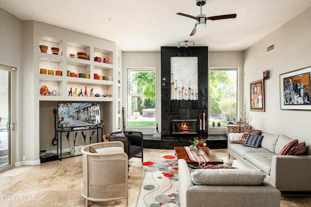 living room with ceiling fan, a fireplace, and built in shelves