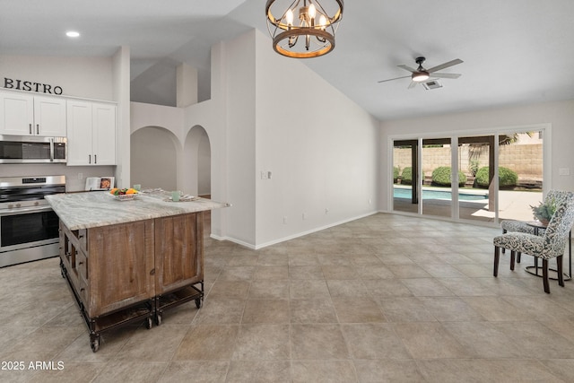kitchen with white cabinets, high vaulted ceiling, ceiling fan with notable chandelier, stainless steel appliances, and a kitchen island