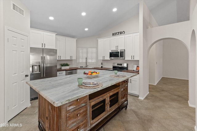 kitchen featuring a sink, arched walkways, stainless steel appliances, vaulted ceiling, and visible vents
