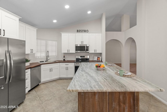kitchen with appliances with stainless steel finishes, arched walkways, a sink, light tile patterned floors, and white cabinets