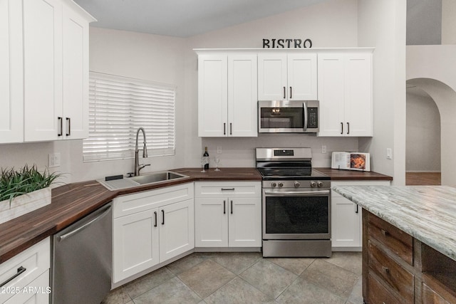 kitchen with a sink, arched walkways, stainless steel appliances, and wood counters