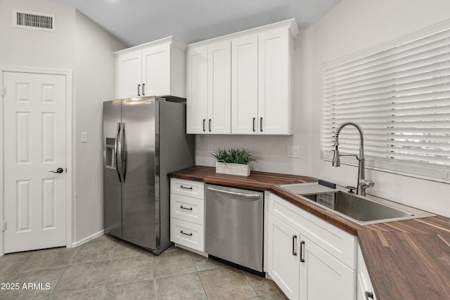 kitchen with white cabinets, appliances with stainless steel finishes, a sink, wooden counters, and visible vents