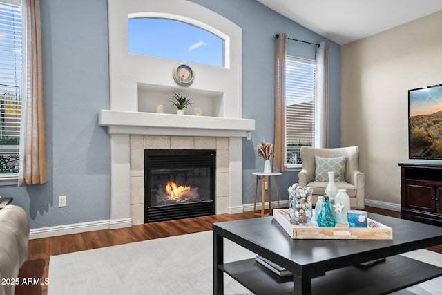 sitting room with a tiled fireplace, baseboards, plenty of natural light, and wood finished floors