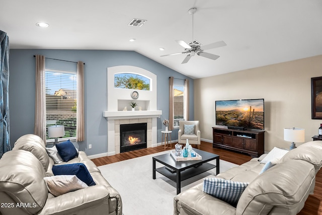 living room with ceiling fan, wood finished floors, a tile fireplace, and vaulted ceiling