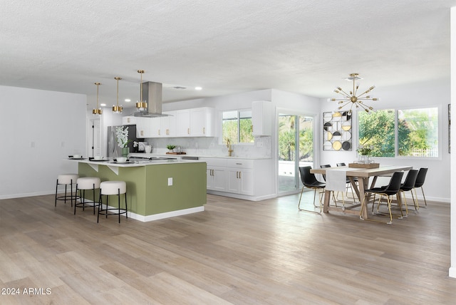 kitchen featuring white cabinets, island exhaust hood, hanging light fixtures, light hardwood / wood-style floors, and a center island