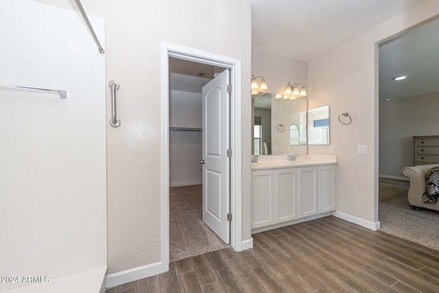 full bathroom with vanity, a walk in closet, wood finished floors, and baseboards