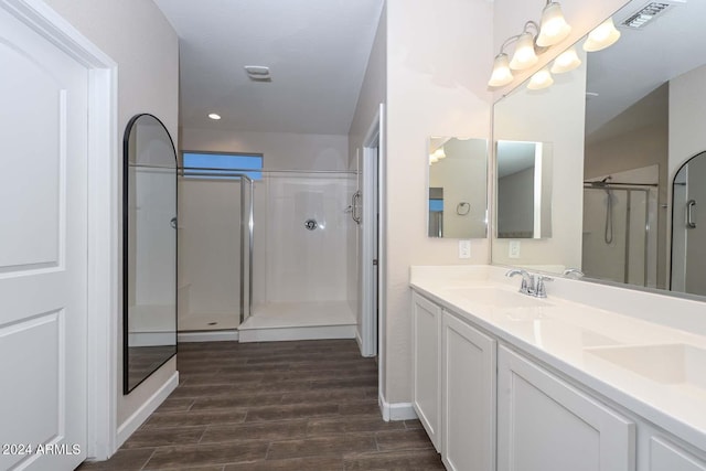 bathroom with visible vents, wood tiled floor, double vanity, a sink, and a shower stall