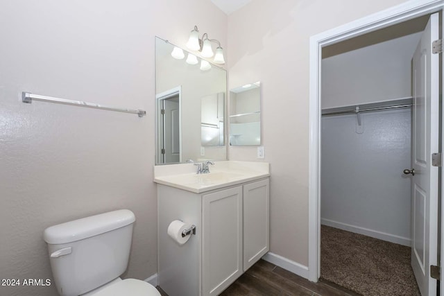 bathroom featuring a spacious closet, baseboards, toilet, wood finished floors, and vanity