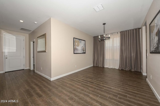 unfurnished room with visible vents, baseboards, dark wood-type flooring, and a notable chandelier