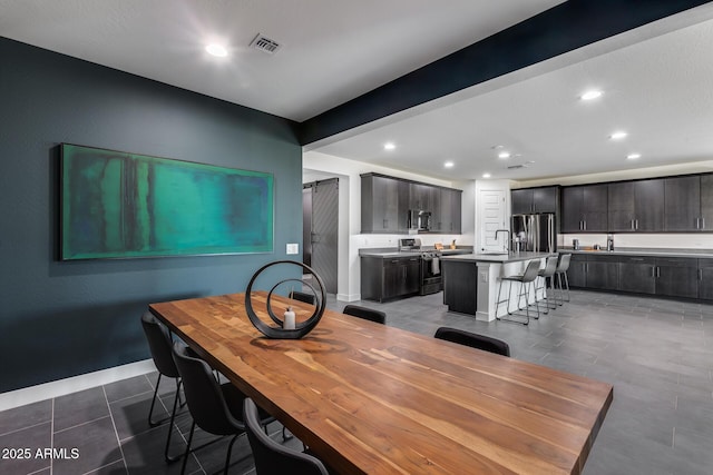 dining room featuring beamed ceiling, a barn door, sink, and dark tile patterned flooring