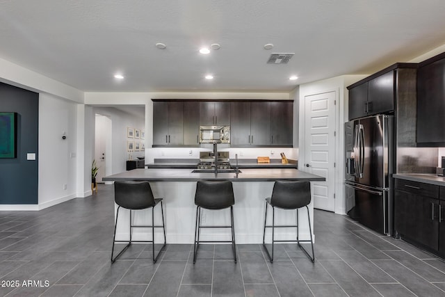 kitchen featuring sink, dark brown cabinets, stainless steel appliances, and an island with sink