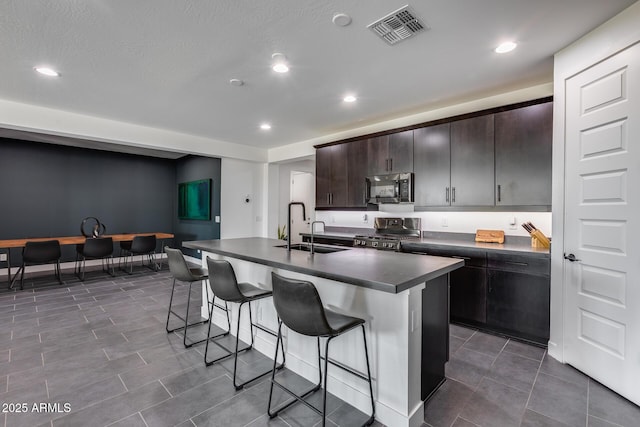 kitchen featuring dark brown cabinetry, sink, a breakfast bar area, range, and a kitchen island with sink