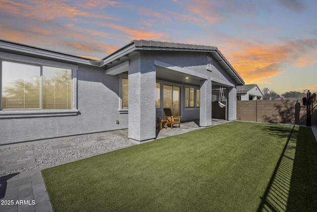 back house at dusk with a lawn and a patio area