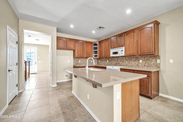 kitchen featuring an island with sink, white appliances, sink, and backsplash