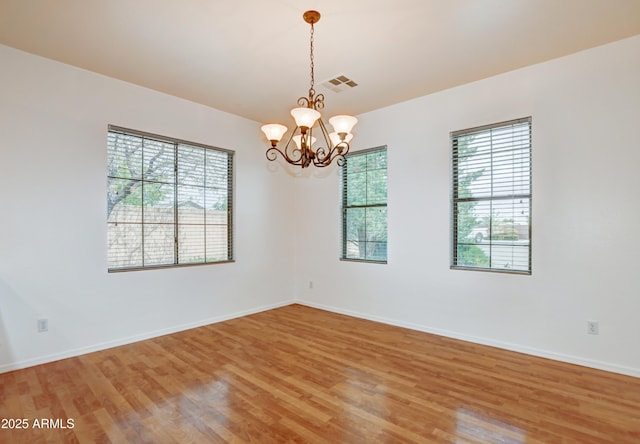 empty room with light wood-style floors, baseboards, an inviting chandelier, and visible vents