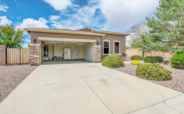 view of front of house featuring fence, an attached garage, stone siding, stucco siding, and driveway