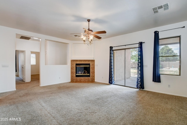 unfurnished living room featuring a tiled fireplace, ceiling fan, carpet flooring, and visible vents