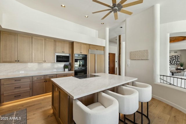 11334 E Troon Vista Dr, Scottsdale, AZ 85255 - kitchen featuring ceiling fan, light wood-style floors, a center island, black appliances, and a breakfast bar area
