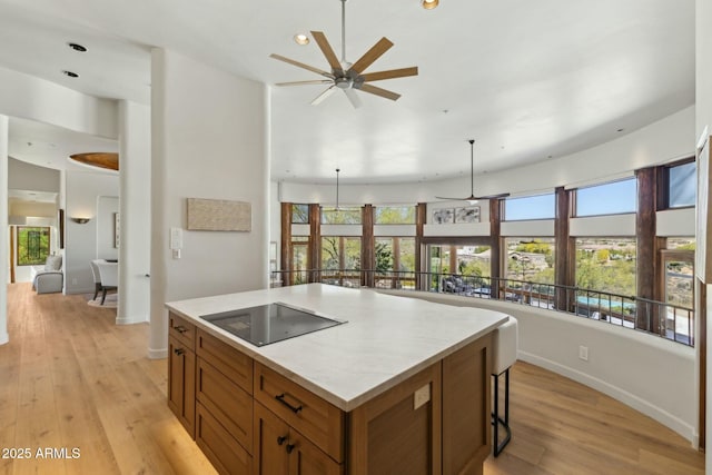 11334 E Troon Vista Dr, Scottsdale, AZ 85255 - kitchen featuring brown cabinets, black electric cooktop, a ceiling fan, a center island, and light wood-style flooring