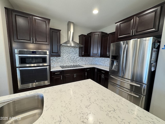 kitchen with appliances with stainless steel finishes, light stone counters, wall chimney range hood, dark brown cabinets, and decorative backsplash