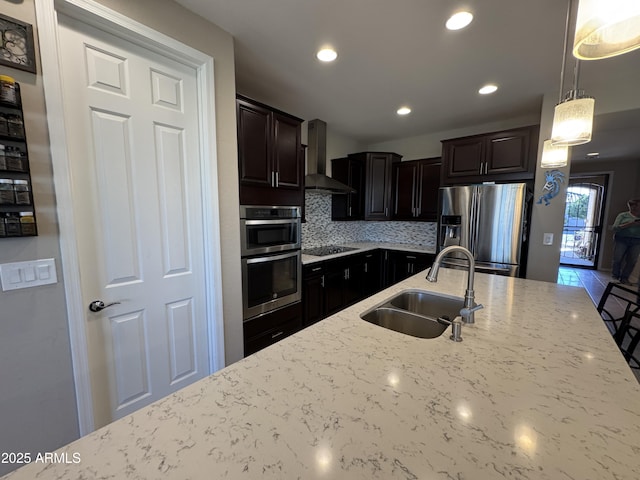 kitchen with sink, pendant lighting, stainless steel appliances, wall chimney exhaust hood, and light stone countertops