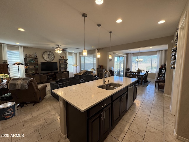 kitchen with an island with sink, light stone counters, stainless steel dishwasher, decorative light fixtures, and sink