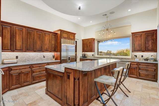 kitchen featuring light stone counters, a towering ceiling, a center island, stainless steel built in refrigerator, and stone tile flooring