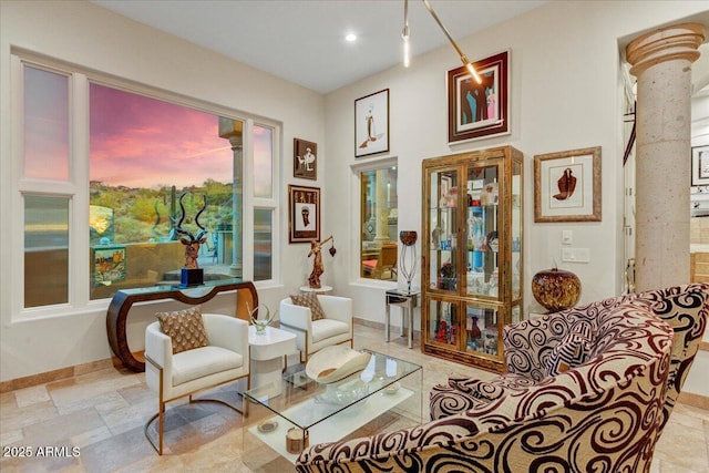 living area featuring recessed lighting, stone finish floor, baseboards, and ornate columns