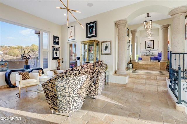 living area featuring decorative columns, stone tile floors, recessed lighting, an inviting chandelier, and baseboards