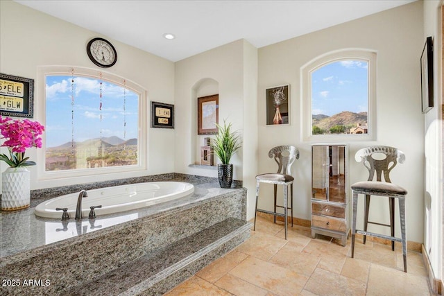 full bath with baseboards, a garden tub, and stone tile floors