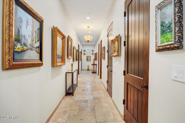 corridor with stone tile floors, baseboards, and a chandelier