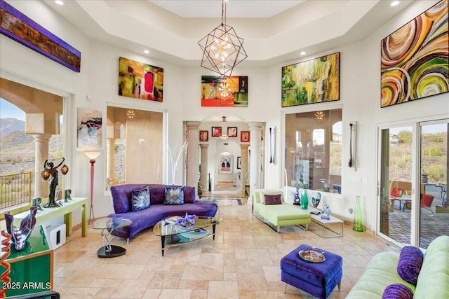 living area featuring arched walkways, a chandelier, a high ceiling, stone finish flooring, and ornate columns